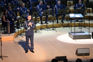 Zdjęcie przedstawia policjanta mówiącego do mikrofonu oraz orkiestrę