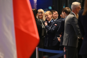 Zdjęcie przedstawia stojących w korytarzy gości oraz policjantkę