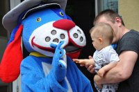 Rodzic trzyma na ręce dziecko, które wita się z policyjną maskotką Sznupkiem