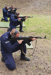 Policjanci strzelają w pozycji klęczącej na trawie